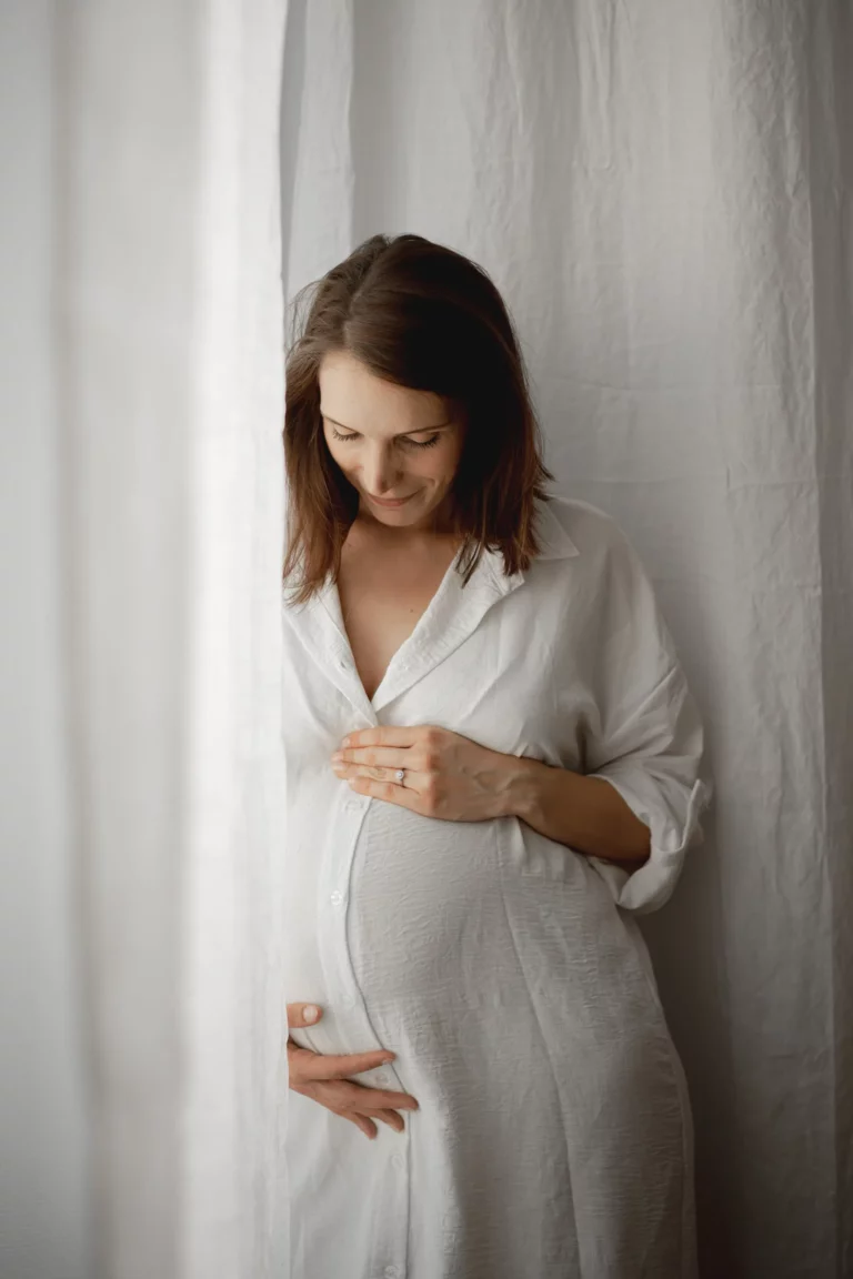 Séance photo de grossesse cocooning à Limoges avec ventre rond adossé à la fenêtre