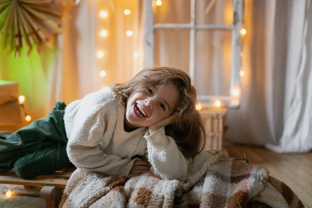 Enfant fille qui rigole lors d'une séance Noël au studio à Limoges devant une décoration avec des couvertures chaudes couchée sur la luge